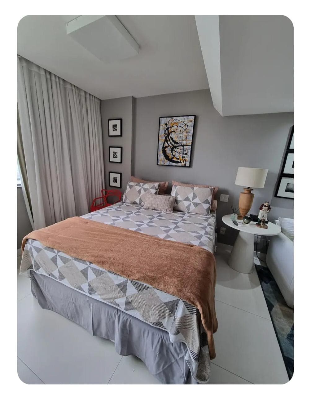 Quarto com cama arrumada, colcha clara e abajur de leitura