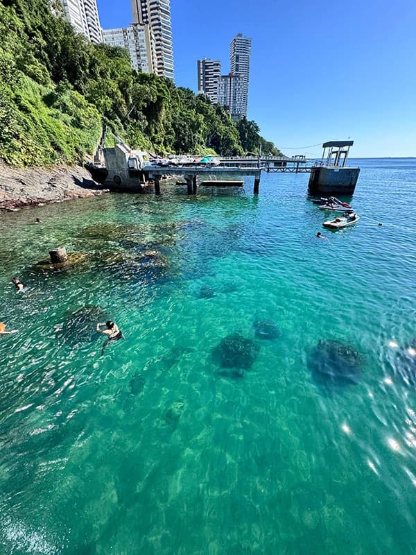 Água cristalina no Píer Mahi Mahi, com jet ski e banhistas e os prédios do Corredor da Vitória ao fundo
